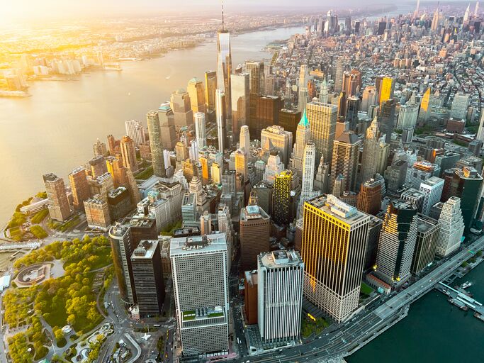 Aerial view of a densely packed urban skyline at sunset, featuring skyscrapers with the sun casting a warm glow over the cityscape.